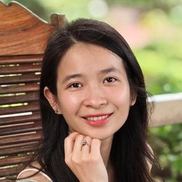Thuỷ Nguyễn smiling, her chin resting on her hand, with a green garden behind her