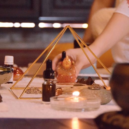 Bàn thực hành chánh niệm với kim tự tháp đồng, nến, hoa sứ, vỏ sò và chuông xoay; một bàn tay đang sắp đặt
