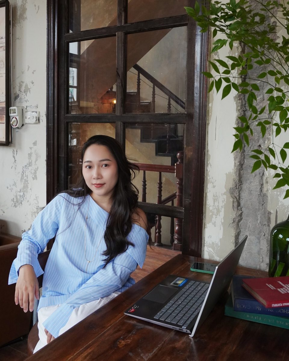 Grace ngồi bên chiếc bàn gỗ cạnh ô cửa sổ kiểu xưa, áo sơ mi xanh nhạt, chiếc laptop mở trước mặt, nhìn thẳng về phía bạn