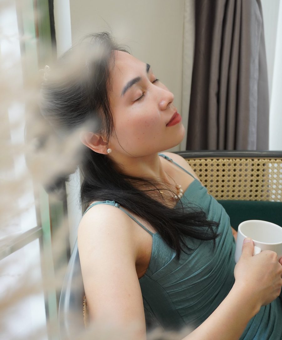 Annie ngả đầu ra sau, mắt khép lại, tay cầm tách trà, ánh nắng chiếu nhẹ lên gương mặt
