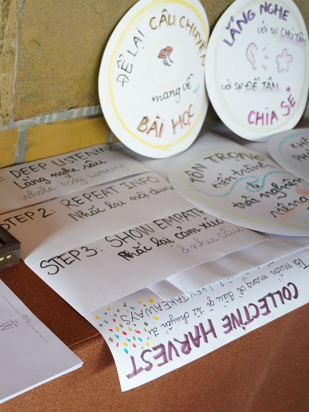 Bàn workshop với những chiếc đĩa viết tay “để lại câu chuyện mang về bài học”, “lắng nghe với sự chú tâm”, “chia sẻ” và tờ giấy “collective harvest”