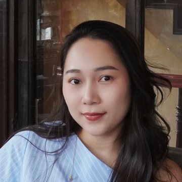 Grace mỉm cười nhìn thẳng, tóc buộc gọn, mặc áo kẻ sọc